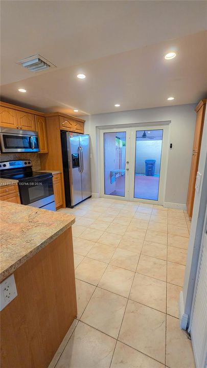 Kitchen featuring wood cabinetry, stone-finish countertops, stainless steel appliances, tile flooring, and glass-paneled double doors