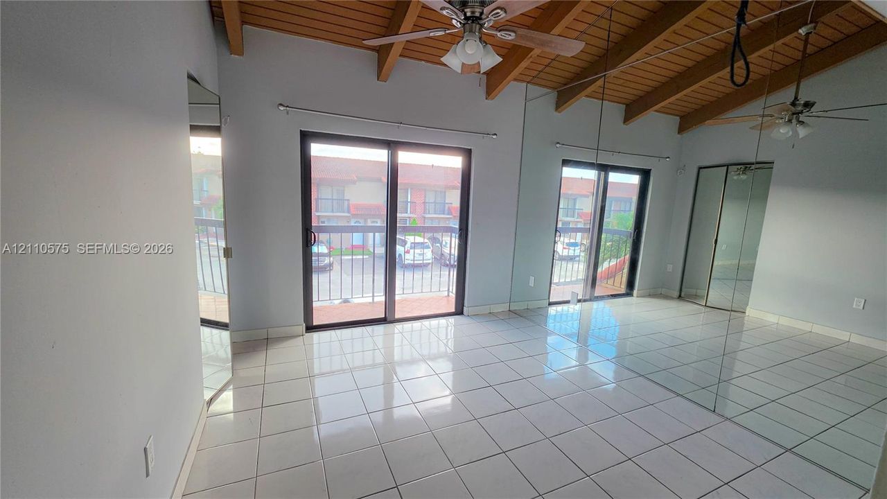 Vaulted ceilings with exposed wooden beams, ceramic tile flooring, dual sliding glass doors, and mirrored closet doors