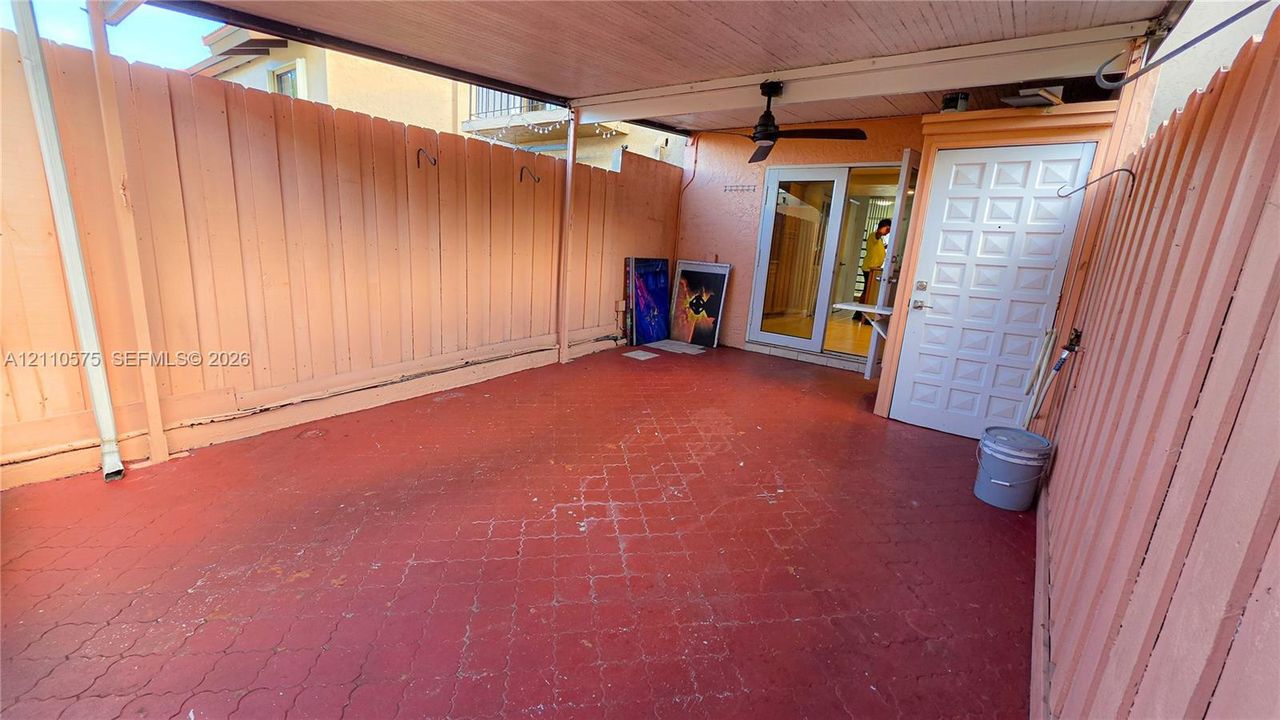 Covered patio area featuring patterned concrete flooring, enclosed by vertical wood fencing, and equipped with a ceiling fan