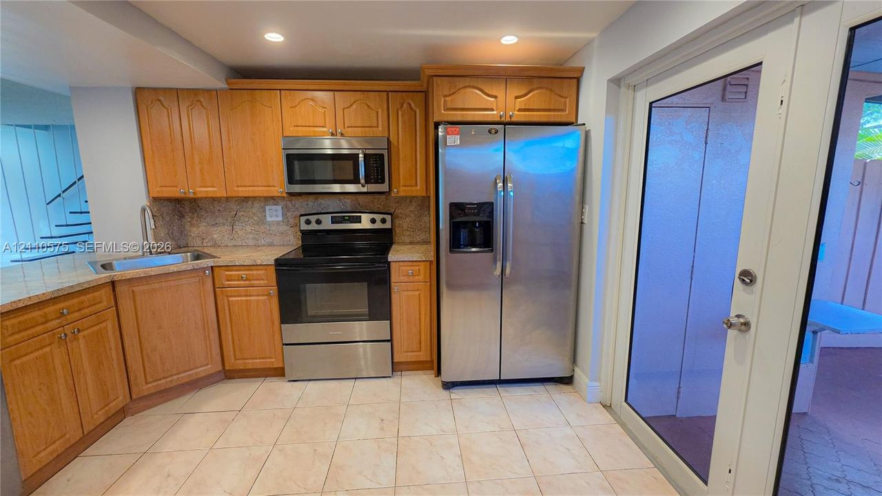 Kitchen featuring natural wood cabinetry, stone countertops, stainless steel appliances, tile flooring, and a full-lite glass exterior door