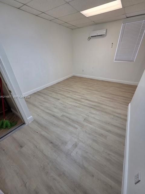 Interior space featuring wood-finish flooring, a wall-mounted ductless mini-split HVAC unit, a drop ceiling with recessed lighting, and a window with horizontal blinds