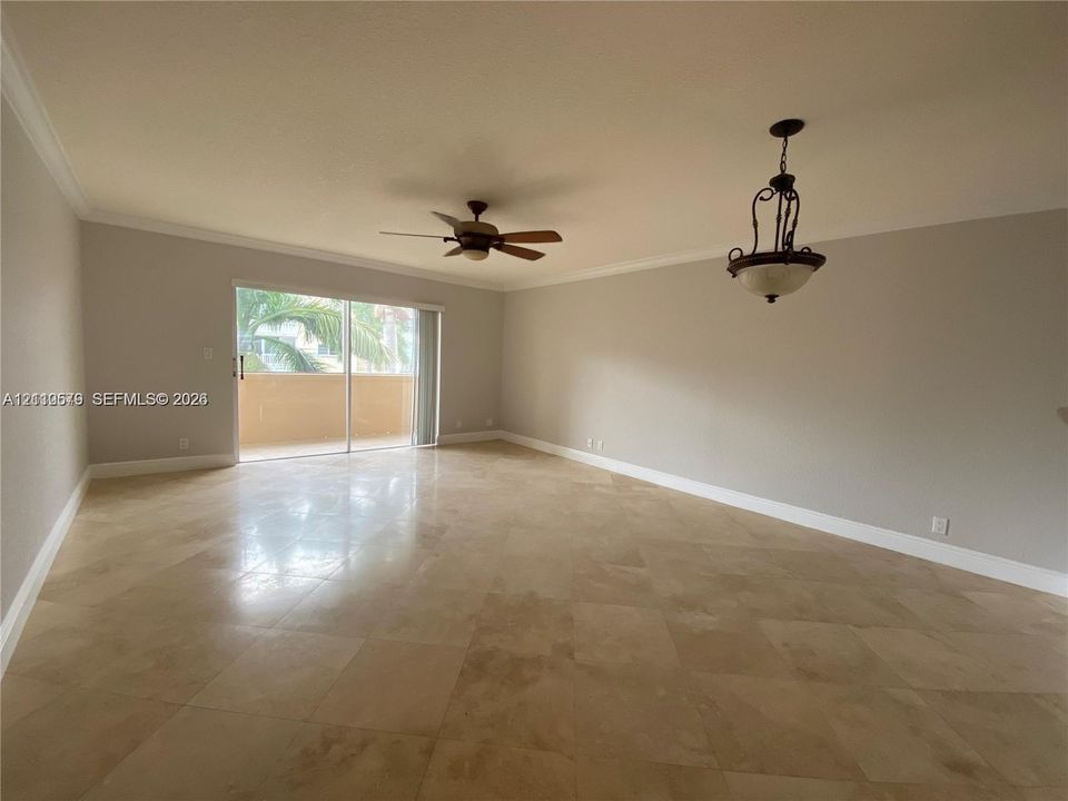 Large room featuring neutral-toned stone-finish flooring, crown molding, a ceiling fan, and a decorative pendant light fixture with sliding glass doors opening to an exterior balcony