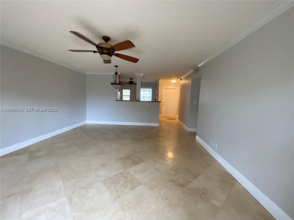 Interior space featuring large-format tile flooring, crown molding, a ceiling fan with integrated lighting, a partial wall partition with a counter surface, and an attached multi-light pendant fixture