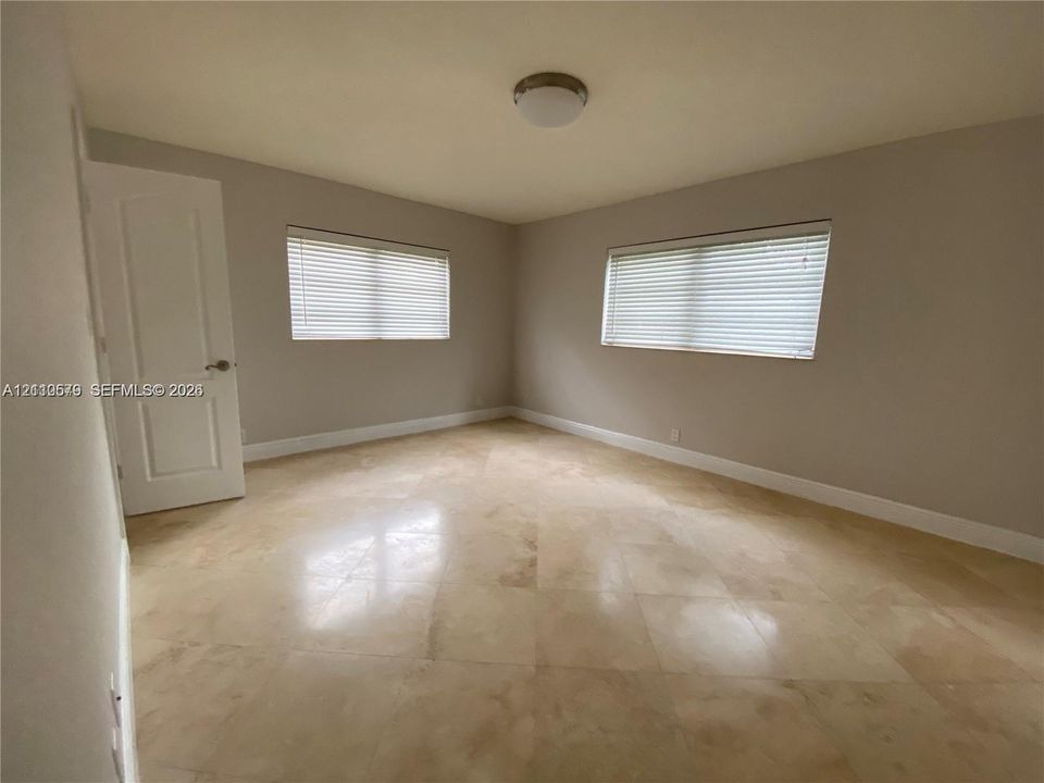 Interior room featuring large-format tile flooring, neutral wall paint, two windows with horizontal blinds, and a paneled interior door