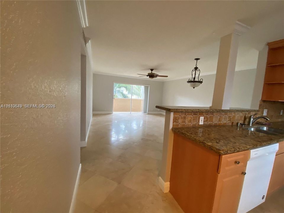 Open-concept interior featuring large-format tile flooring, a kitchen peninsula with stone-finish countertops, decorative tile backsplash, recessed ceiling fan, and sliding glass doors