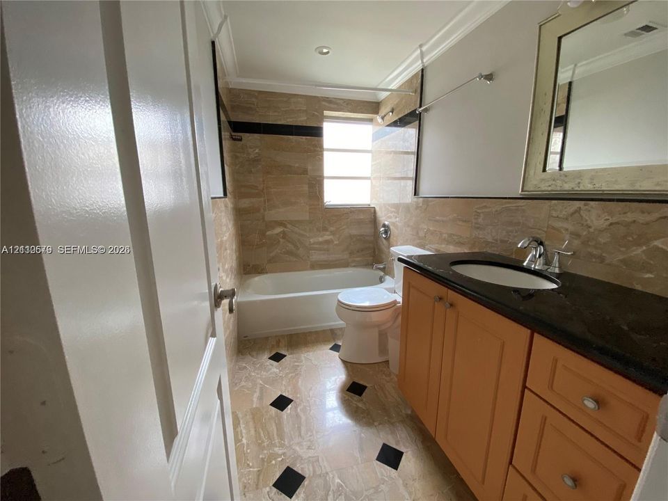 Bathroom featuring stone tile flooring with decorative black insets, a vanity with a dark countertop and integrated sink, stone-tiled wall surrounds, and a porcelain soaking tub