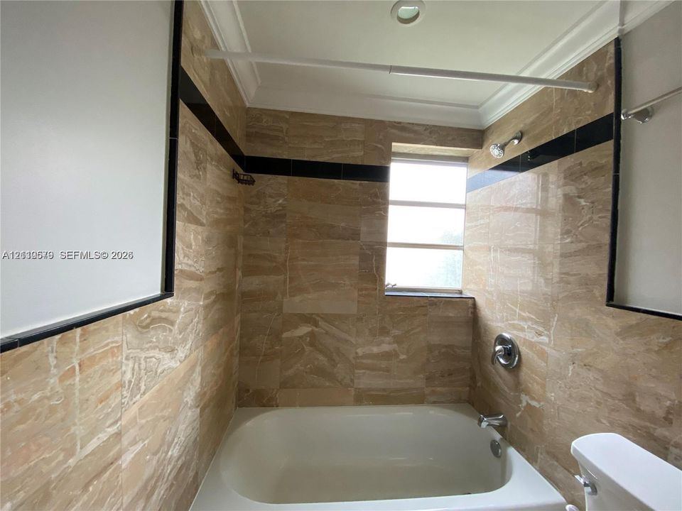 Full-height natural-tone stone wall tiling with contrasting black accent trim, integrated bathtub, and polished metal shower fixtures