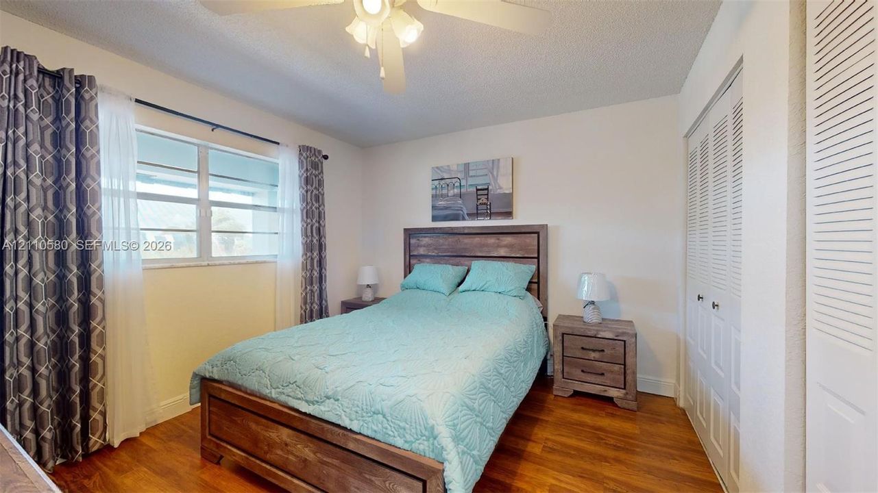 Wood-finish flooring, horizontal sliding windows, ceiling fan with integrated lighting, and dual louvered-door closets