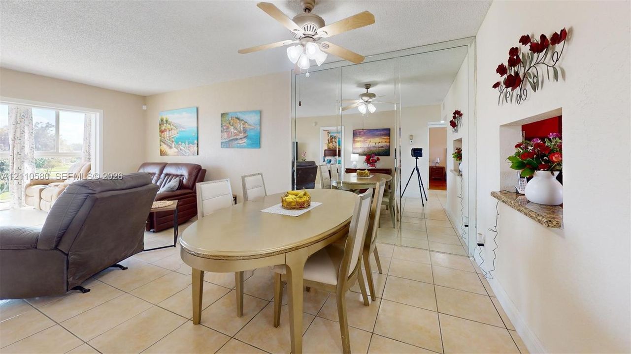 Open-concept area featuring neutral tile flooring, mirrored wall paneling, a ceiling fan with integrated lighting, and a built-in recessed wall niche with a stone-finish ledge