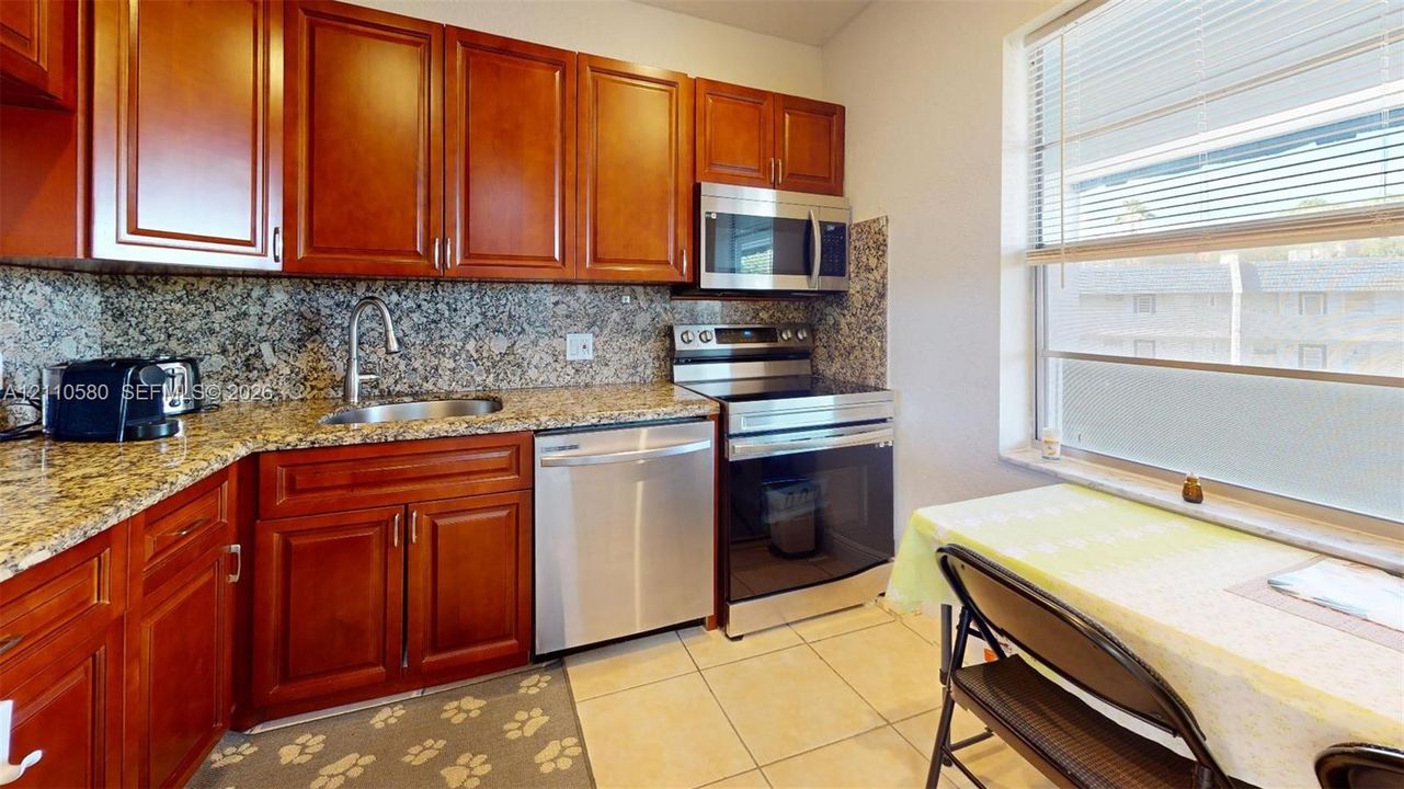 Kitchen featuring cherry-finish cabinetry, stone-surface countertops, stone tile backsplash, stainless steel appliances, and tile flooring