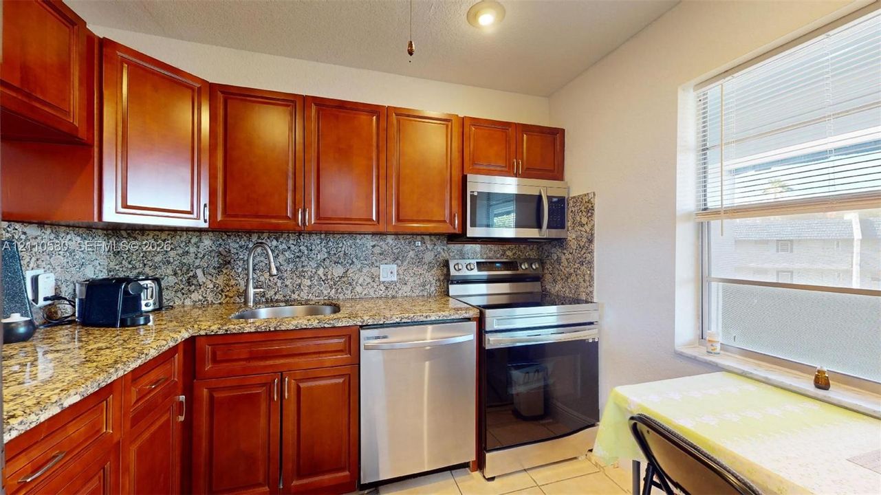 Kitchen featuring wood cabinetry, stone countertops, stone tile backsplash, stainless steel appliances, and a window