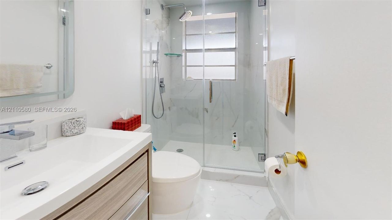 Modern bathroom featuring a wood-finish floating vanity, integrated rectangular sink, walk-in shower with glass enclosure, and light-toned tile flooring