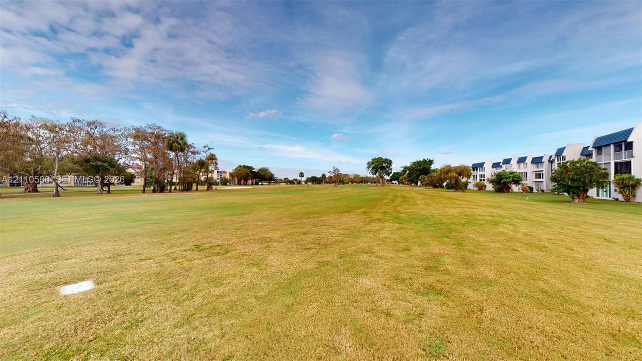 Expansive grounds featuring a vast manicured lawn, scattered mature trees, and multi-story residential buildings