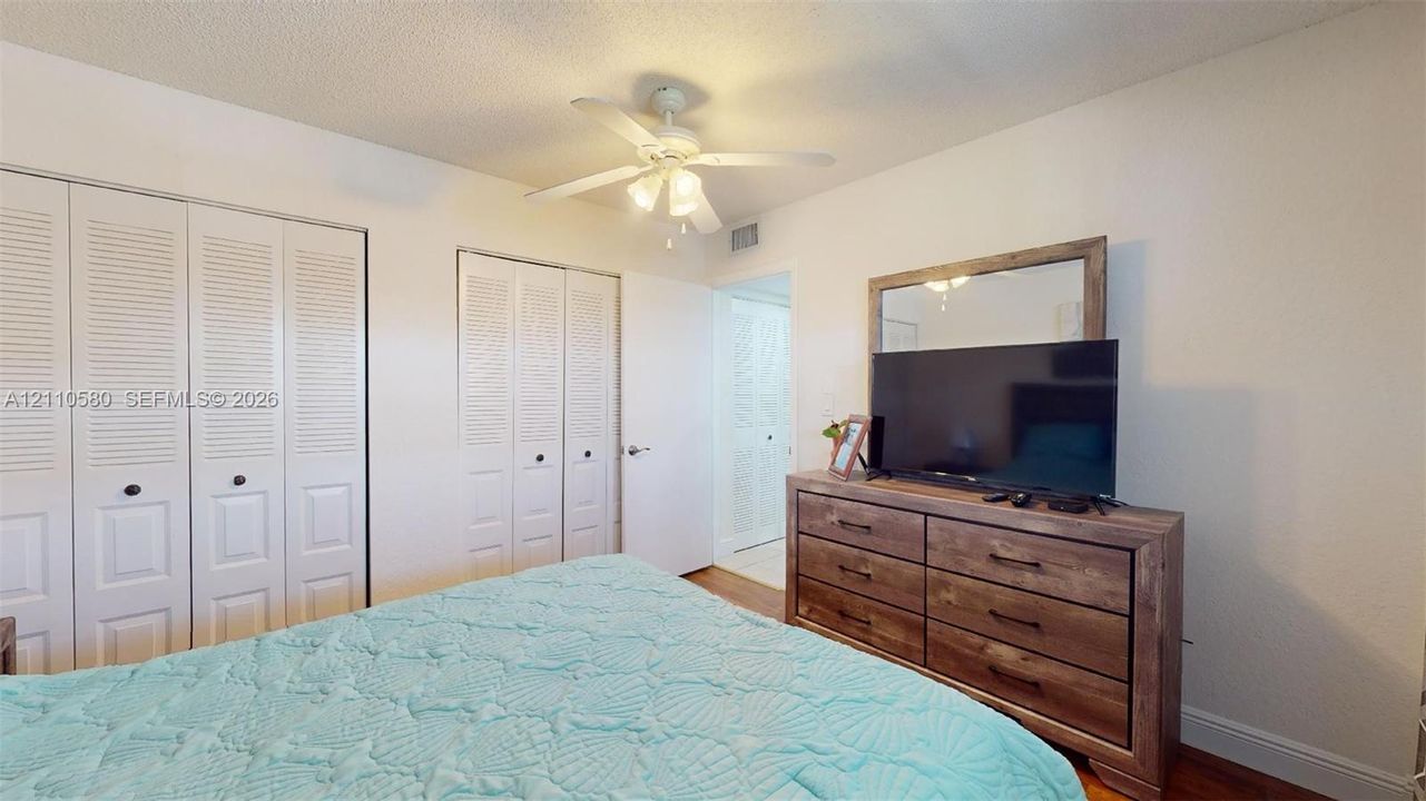 Room featuring dual sets of white louvered-panel closet doors and a central ceiling fan with integrated lighting