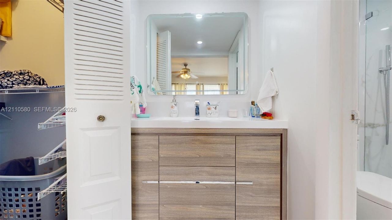 Wood-finish vanity cabinet, integrated sink, rectangular wall-mounted mirror, and glass-enclosed shower