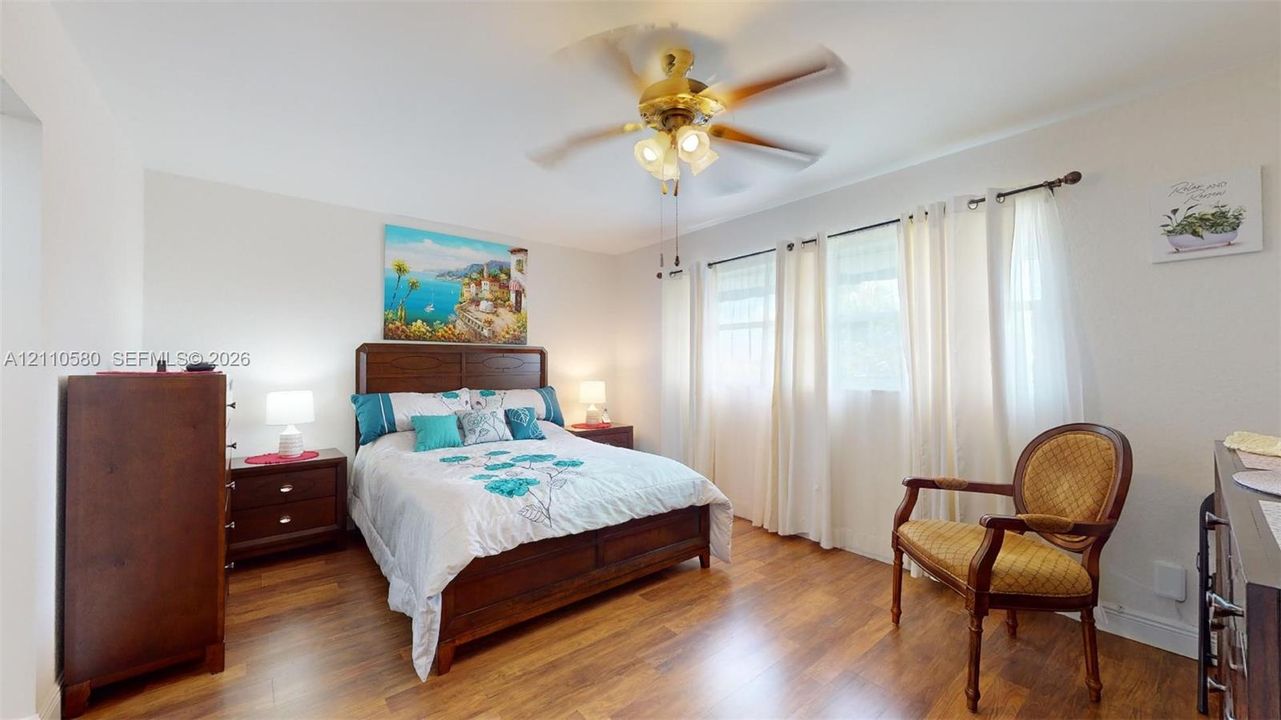 Room featuring wood-finish flooring, a multi-blade ceiling fan with integrated lighting, and large windows with horizontal blind hardware