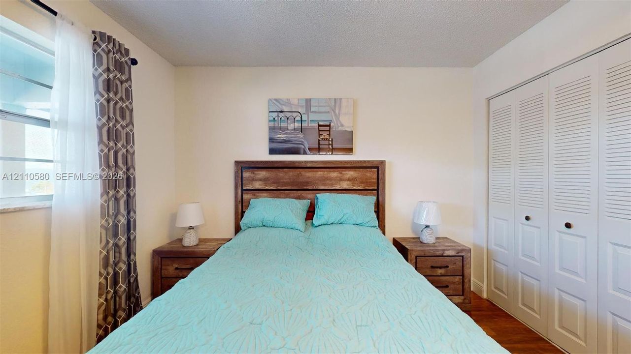 Bedroom featuring wood-finish flooring, dual-panel louvered closet doors, and a window with horizontal blinds