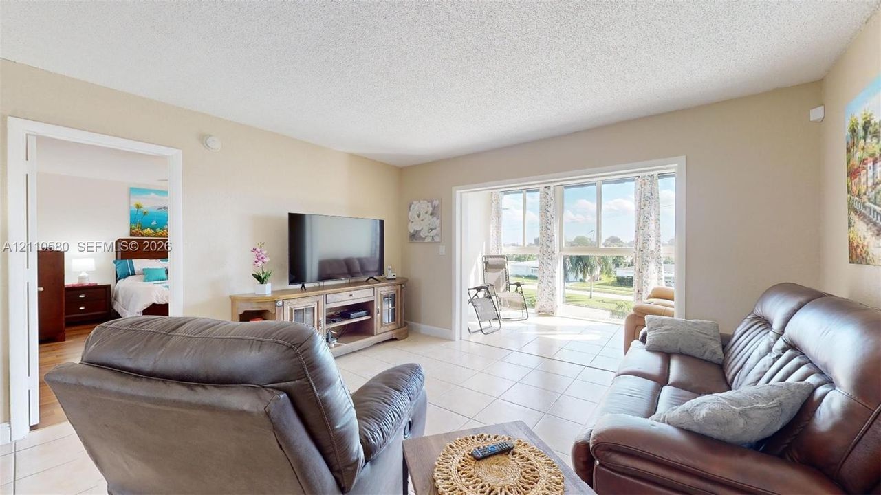 Living area featuring large-format tile flooring, neutral wall paint, and a sliding glass door providing natural light