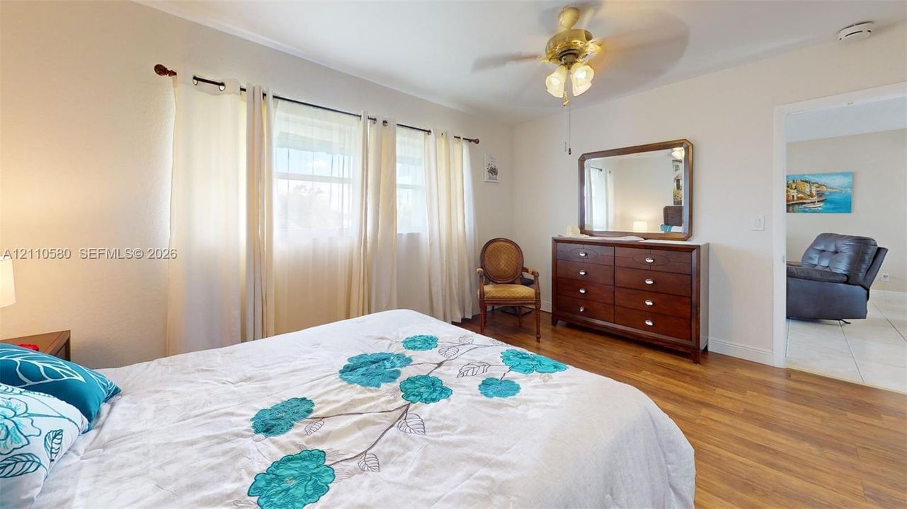 Bedroom featuring wood-finish flooring, multiple windows with curtain rod hardware, and a ceiling-mounted light fixture with fan