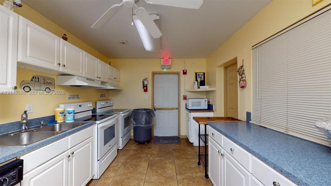 Kitchen featuring white cabinetry, solid-surface countertops, dual stainless steel sinks, and tile flooring