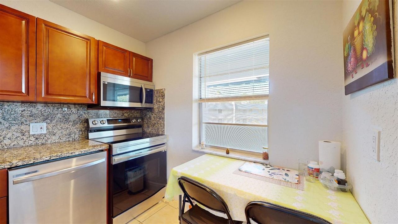 Kitchen featuring warm-tone wood cabinetry, stone-patterned countertops, stainless steel appliances, and a window for natural light