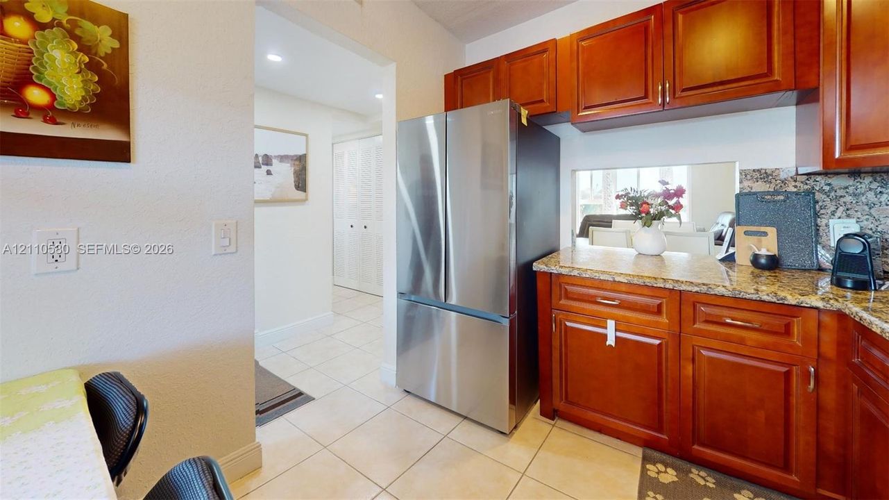 Kitchen featuring stained wood cabinetry, stone countertops, stainless steel refrigerator, and tiled flooring