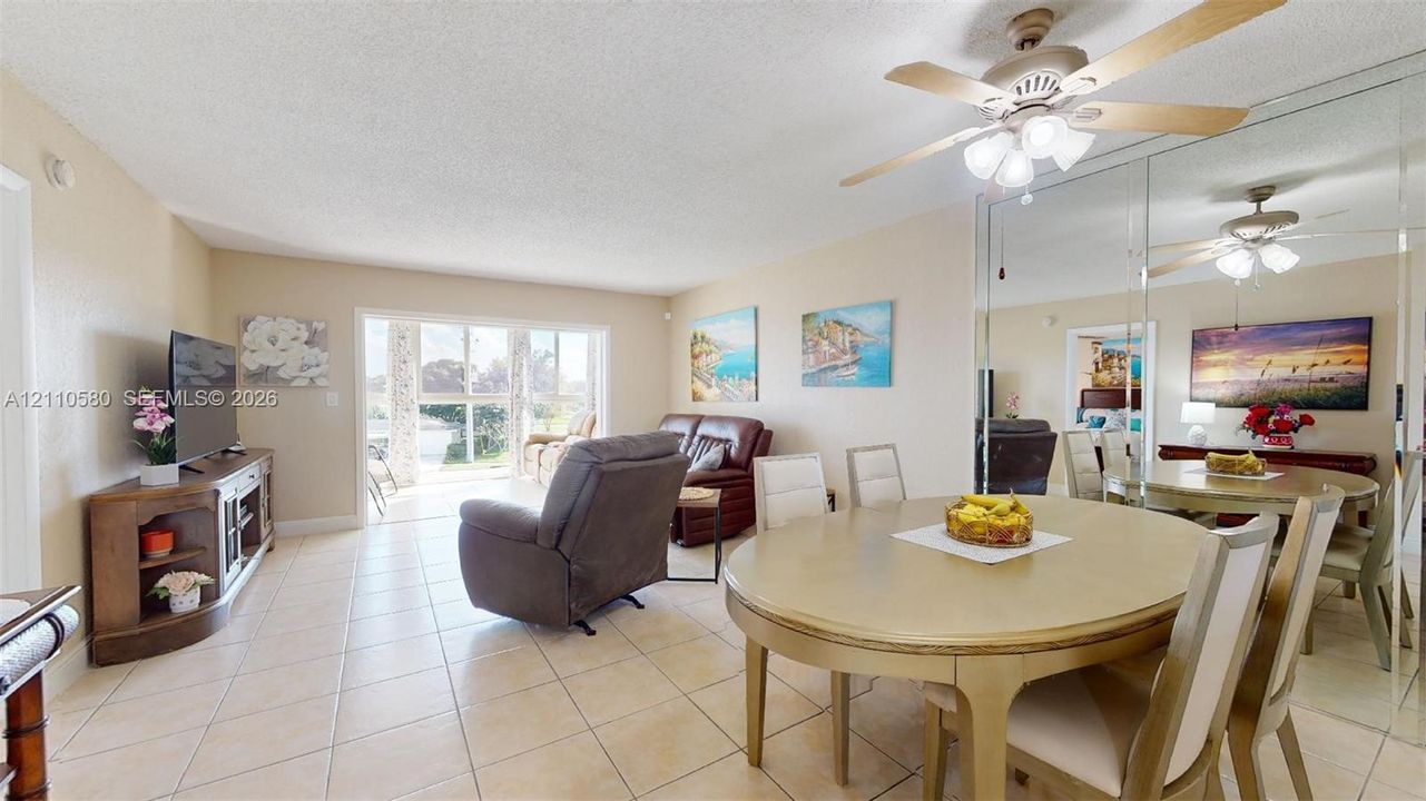 Open living area featuring neutral tile flooring, expansive glass doors, a wall of floor-to-ceiling mirror panels, and a ceiling-mounted light fixture with a fan