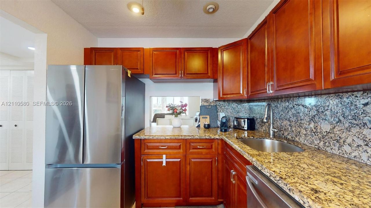 Kitchen featuring stained wood cabinetry, stone countertops, stone backsplash, stainless steel refrigerator, and stainless steel sink