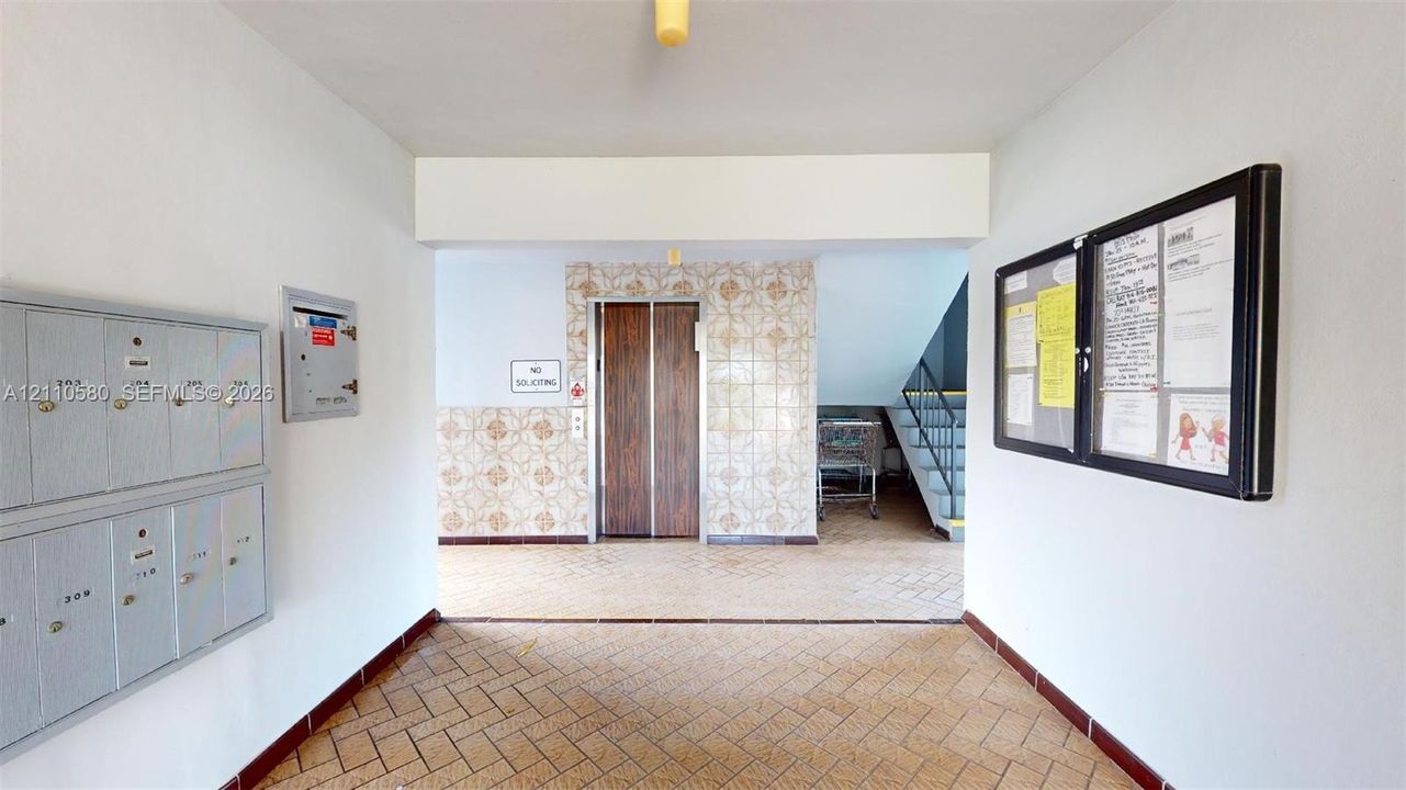 Common area lobby featuring terra-cotta style tile flooring, patterned ceramic wall tile, metallic mailboxes, and an elevator