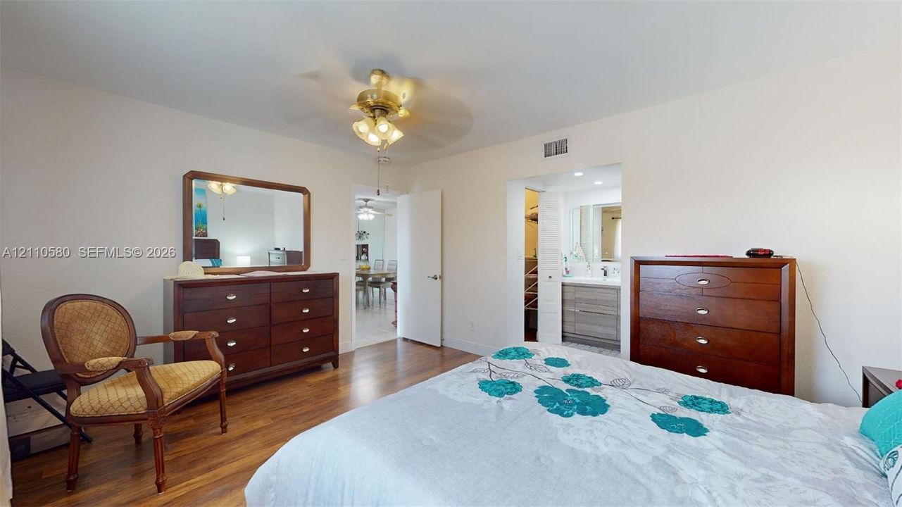 Room featuring wood-finish flooring, a multi-light ceiling fan, and access to a secondary space with a vanity