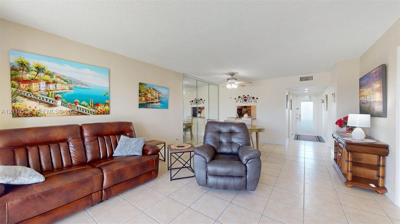 Living area featuring light-toned tile flooring, mirrored sliding-door closet, and ceiling fan with integrated lighting