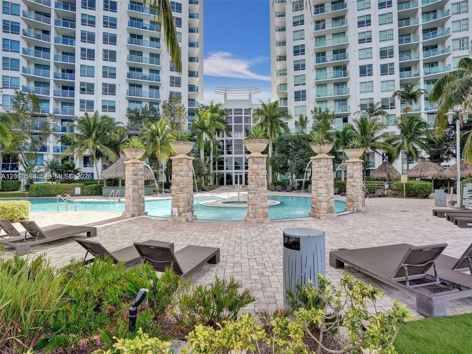 Swimming pool area featuring stone-clad pillars, a paved deck, and mature palm trees