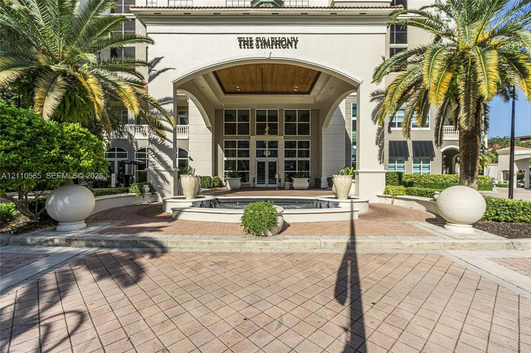 Covered porte-cochère entry featuring a stone-paved motor court, central water fountain, and wood-paneled ceiling detailing