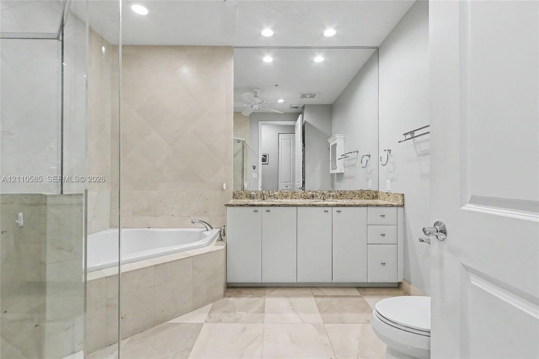 Main Bathroom featuring a double-sink vanity with stone countertop, corner soaking tub with tile surround, glass-enclosed shower, and large wall-mounted mirror