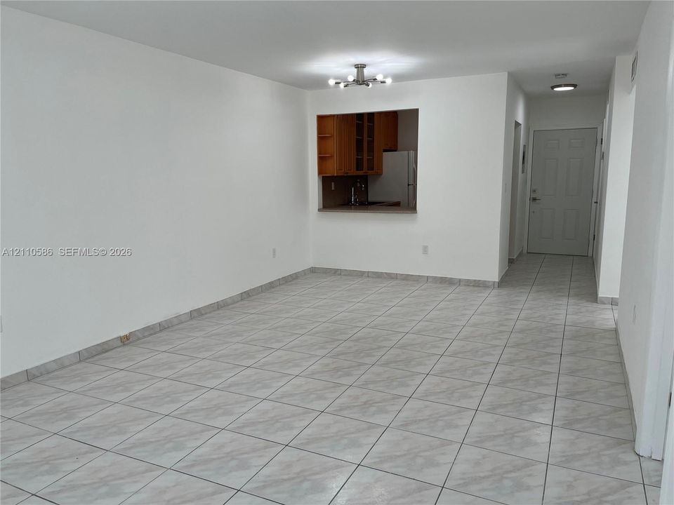 Open interior featuring neutral wall finishes, tile flooring, a multi-arm overhead light fixture, and a pass-through window to the kitchen area