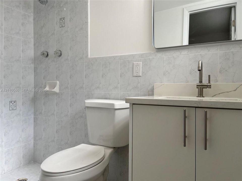 Bathroom featuring a light-toned vanity with a solid-surface countertop, an undermount sink with a single-handle faucet, a wall-mounted mirror, and floor-to-ceiling tile work within the shower enclosure