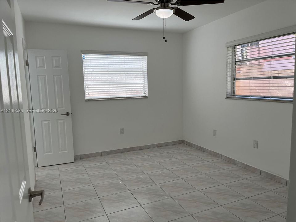Interior space featuring neutral wall tones, large-format tile flooring, dual windows, and a ceiling-mounted light fixture with a multi-blade fan