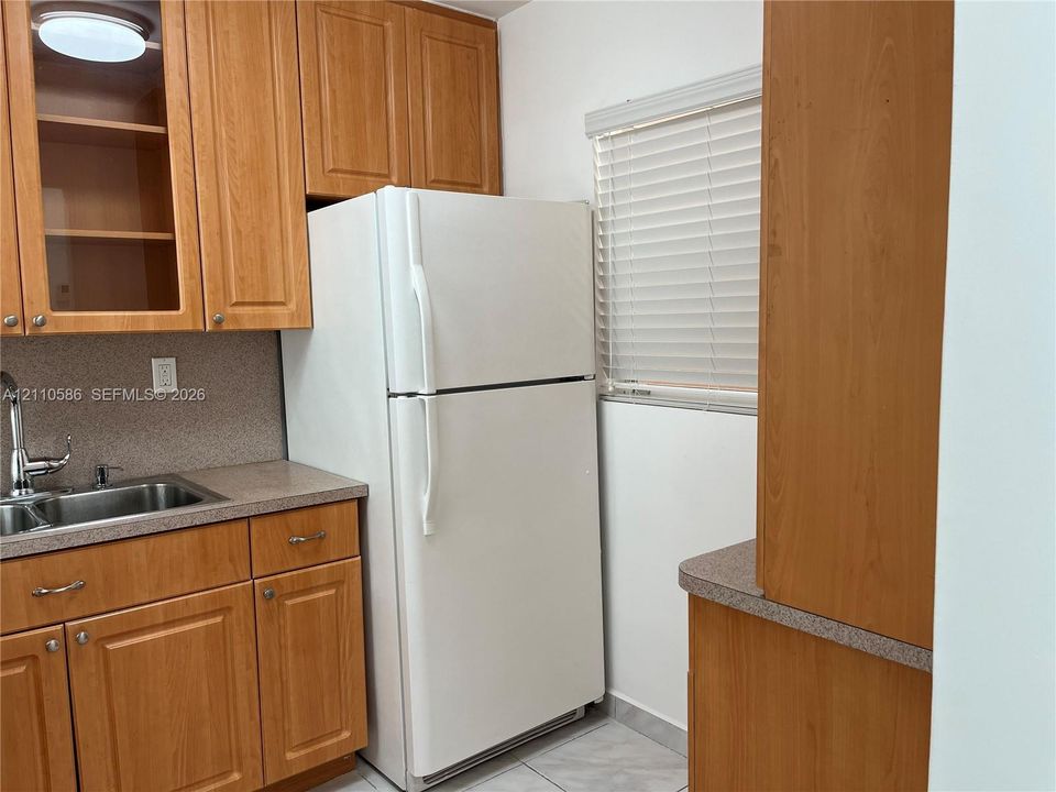 Kitchen featuring wood-finish cabinetry, stainless steel sink with a chrome faucet, solid-surface countertops, and tile flooring