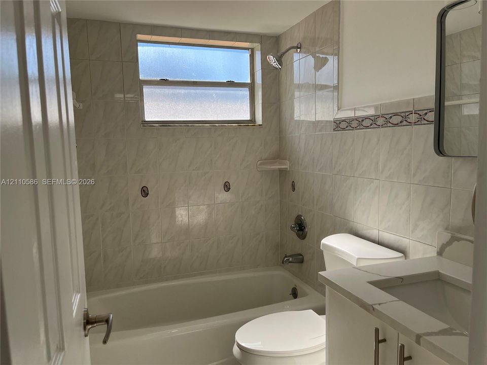 Bathroom featuring a tub-shower combination with tiled surround, stone-composite countertop, undermount sink, and polished chrome hardware