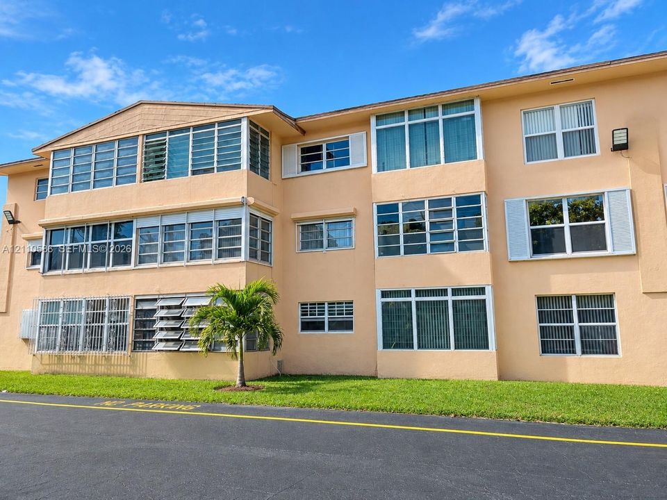 Multi-story stucco exterior featuring horizontal sliding windows, louvered window panels, decorative shutters, and manicured turf