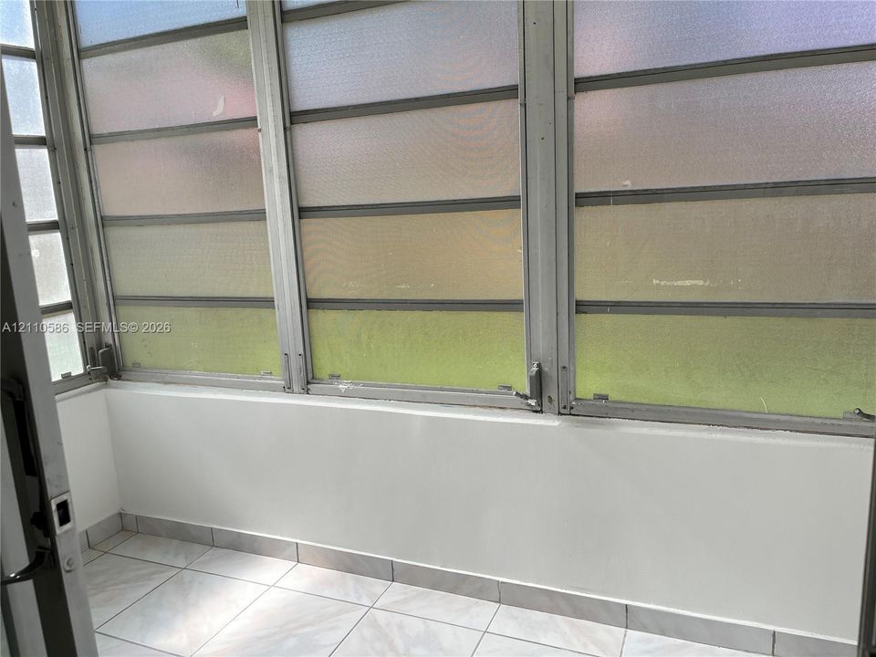 Enclosed sunroom featuring light-toned tile flooring, solid wall paneling, and multiple aluminum-framed jalousie windows