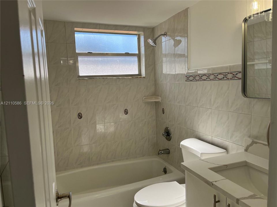 Bathroom featuring a vanity with a stone-finish countertop, under-mount sink, tile-surround shower and tub combination, and horizontal window