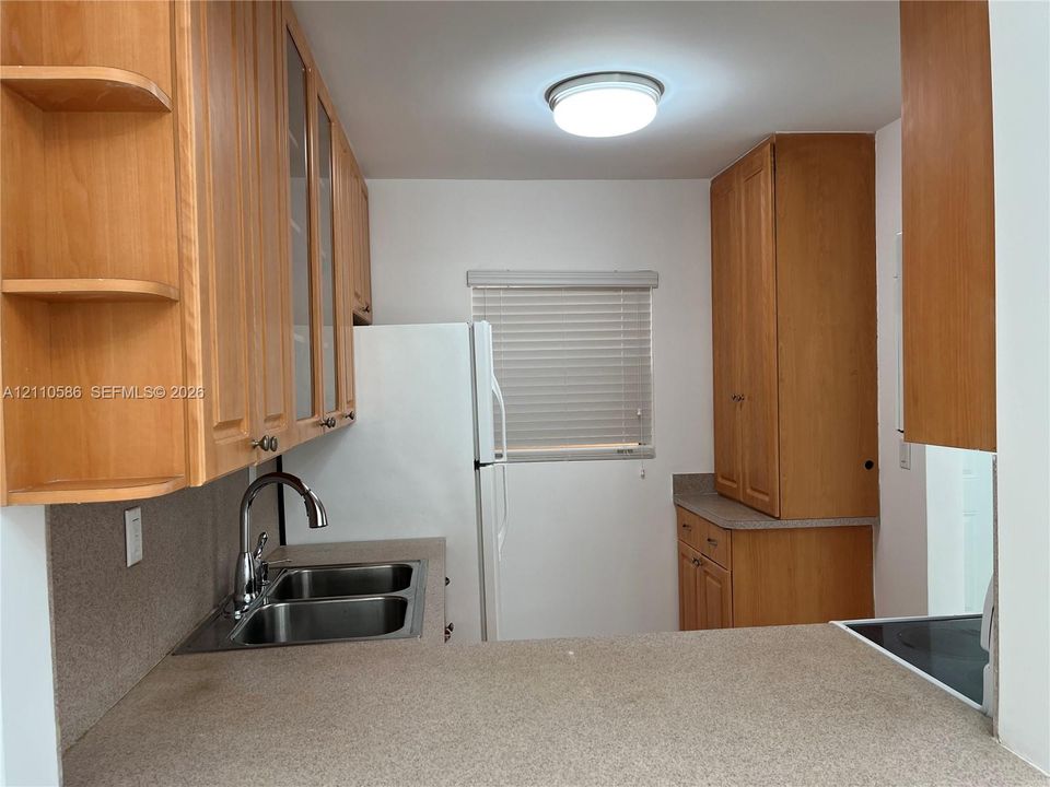 Kitchen featuring wood cabinetry with glass-panel upper doors, solid-surface countertops, dual-basin stainless steel sink with high-arc faucet, and overhead flush-mount lighting