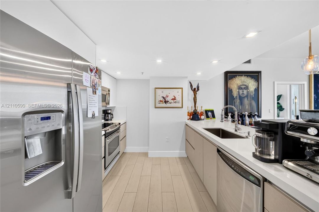 Modern kitchen featuring stainless steel appliances, flat-panel cabinetry, light-toned countertops, an integrated sink with a gooseneck faucet, and wood-finish flooring