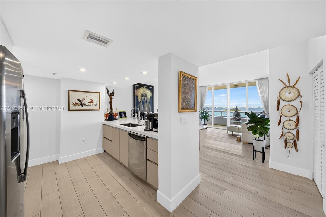 Kitchen featuring light-toned cabinetry, stainless steel appliances, solid-surface countertops, wood-finish flooring, and floor-to-ceiling glass sliding doors