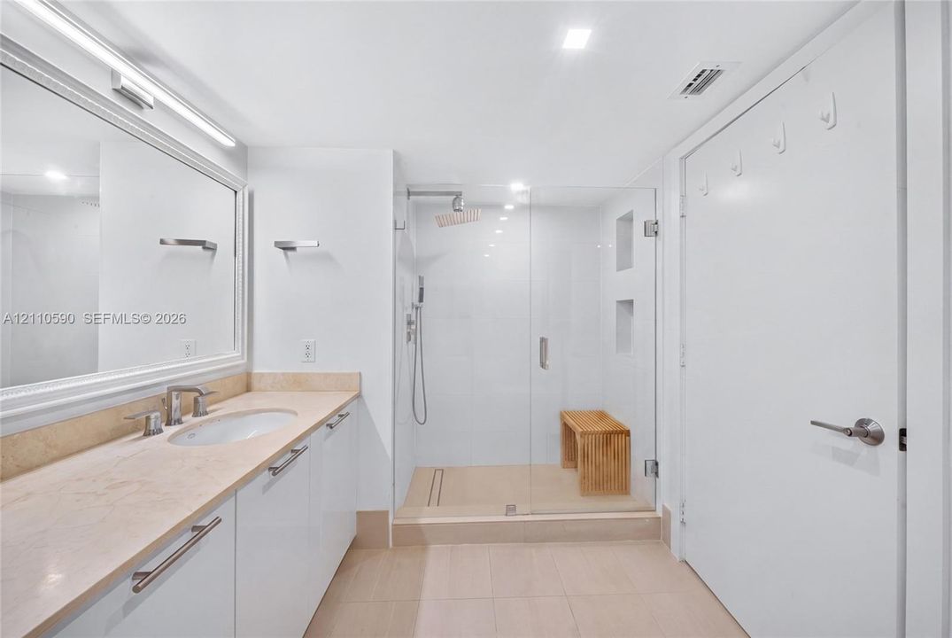 Bathroom featuring a stone-topped vanity with an integrated basin, a large wall-mounted mirror, a walk-in shower with a glass enclosure, and recessed shower wall niches