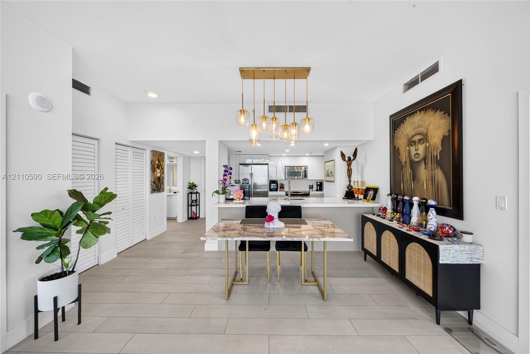 Open floor plan featuring wood-finish tile flooring, a gold multi-pendant light fixture, a quartz-topped breakfast bar, and white louvered closet doors