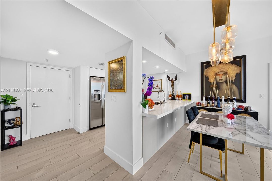 Wood-finish flooring, stone-surfaced breakfast bar, recessed ceiling lighting, multi-globe pendant light fixture, and stainless steel refrigerator