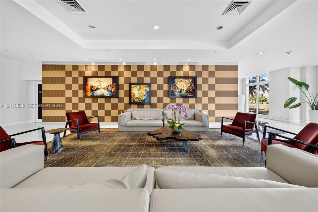 Common area featuring a checkerboard-pattern wood accent wall, recessed tray ceiling, and polished large-format tile flooring
