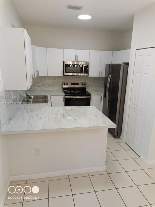 Kitchen featuring white cabinetry, stone-patterned countertops, stainless steel appliances, a dual-basin sink, and ceramic tile flooring